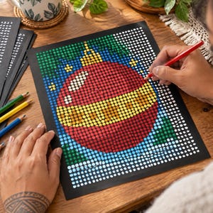 May include: A dot-to-dot coloring sheet on black paper featuring a large red and yellow Christmas ornament design. The artwork is composed of a grid of white circles, some of which are filled with red, yellow, green, and blue colors.