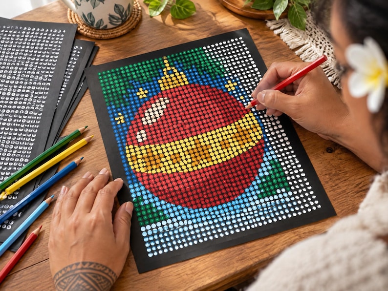 May include: A dot-to-dot coloring sheet on black paper featuring a large red and yellow Christmas ornament design. The artwork is composed of a grid of white circles, some of which are filled with red, yellow, green, and blue colors.