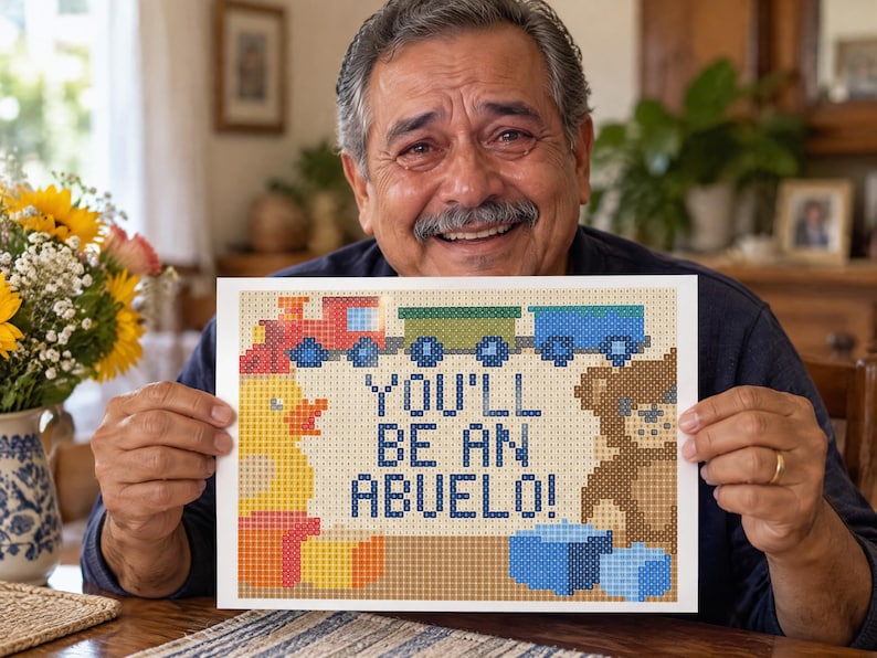 Puede incluir: Una impresi&oacute;n rectangular con un dise&ntilde;o de arte de p&iacute;xeles que muestra un tren rojo, un pato amarillo y un oso de peluche marr&oacute;n. El texto central dice YOU'LL BE AN ABUELO! en letras may&uacute;sculas azul oscuro sobre un fondo de rejilla beige.