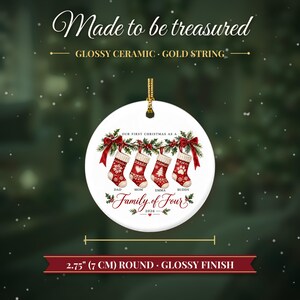 May include: A 2.75-inch round glossy ceramic ornament with a gold string. The design features four red and white Christmas stockings hanging from a garland with the text "OUR FIRST CHRISTMAS AS A FAMILY OF FOUR" and "2026".