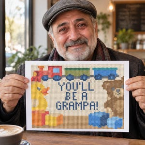 Puede incluir: Un letrero rectangular blanco con un diseño de arte de píxeles que muestra un tren rojo, un patito de goma amarillo y un oso de peluche marrón. El texto en el centro del letrero dice "YOU'LL BE A GRAMPA!" en letras pixeladas de color azul oscuro.