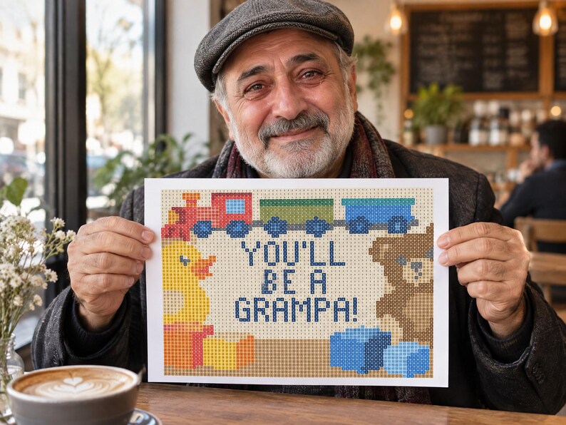 May include: A rectangular white sign featuring a pixel art design of a red train, a yellow rubber duck, and a brown teddy bear. The text in the center of the sign reads, "YOU'LL BE A GRAMPA!" in dark blue pixelated letters, surrounded by colorful blocks.