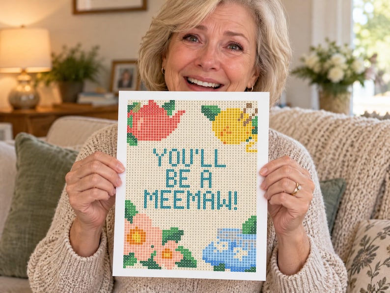 May include: A rectangular print featuring a pixelated design with the text YOU'LL BE A MEEMAW! in blue. The design includes a red teapot, a yellow lemon, pink flowers with green leaves, and a blue teacup on a light beige grid background.
