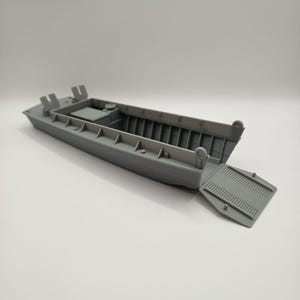 Könnte beinhalten: Graues Modell eines Landungsbootes mit abgesenkter Rampe vorne. Das Boot weist detaillierte Merkmale auf, darunter Innenstützen und eine kleine Plattform. Das Gesamtdesign ist eine Miniaturreplik eines Militärschiffs.