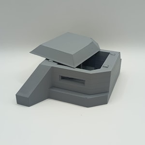 Peut inclure: Modèle gris imprimé en 3D d'un bunker militaire avec un toit articulé. Le bunker a une forme rectangulaire avec une entrée en pente et une petite ouverture rectangulaire. Le toit est partiellement ouvert.