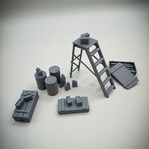 Op de afbeelding: Een verzameling miniatuur grijze industriële modellen, waaronder vaten, brandstofcontainers, kisten en een trap. De items zijn gerangschikt op een lichtgrijze ondergrond, wat wijst op een bouw- of industrieel thema.
