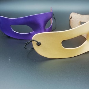 Puede incluir: Dos m&aacute;scaras de carnaval, una morada y otra beige, con cintas el&aacute;sticas negras.