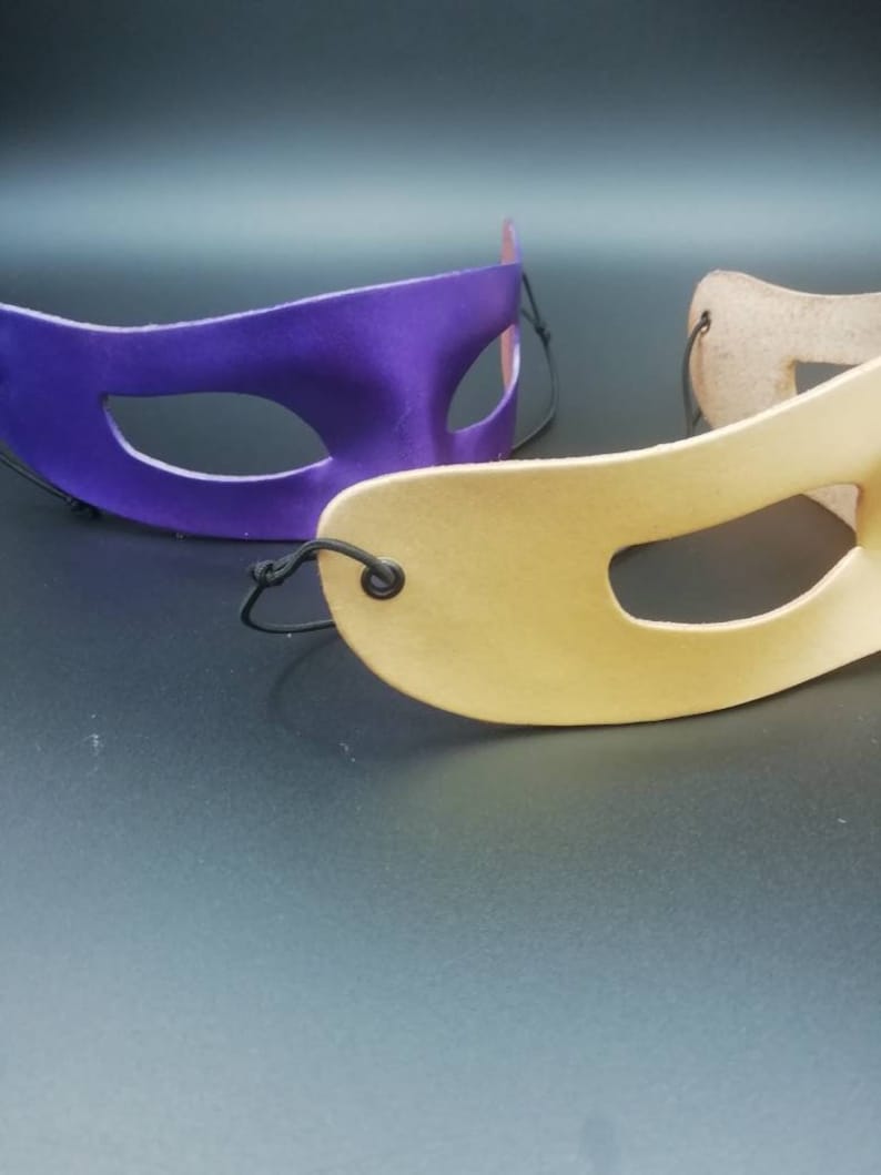 Puede incluir: Dos m&aacute;scaras de carnaval, una morada y otra beige, con cintas el&aacute;sticas negras.