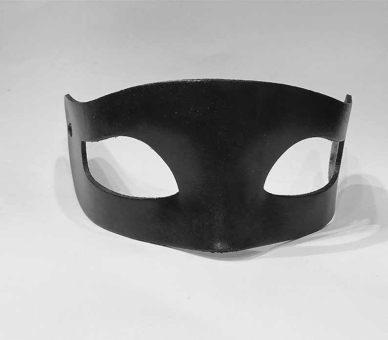 Puede incluir: Una m&aacute;scara para los ojos de cuero negro con dos agujeros para los ojos. La m&aacute;scara es curva y tiene un dise&ntilde;o simple.
