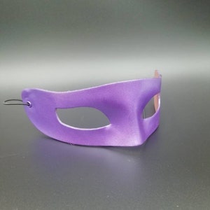 Puede incluir: M&aacute;scara de carnaval morada con un solo agujero para el ojo. La m&aacute;scara est&aacute; hecha de un material liso y brillante y tiene un dise&ntilde;o simple y elegante.