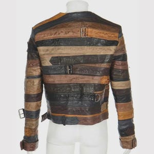 Puede incluir: Chaqueta de cuero multicolor con tiras horizontales en tonos marr&oacute;n, negro y beige. La chaqueta tiene m&uacute;ltiples hebillas y correas. Se muestra la vista trasera de la chaqueta.