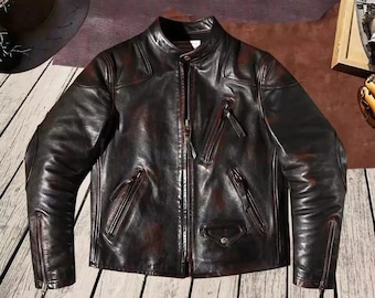 Pode incluir: Casaco de couro castanho escuro com gola alta e múltiplos bolsos com zíper. O casaco tem um estilo motociclista clássico com um acabamento desgastado, mostrando uma estética vintage. O casaco apresenta um fecho frontal com zíper e zíperes nas mangas.