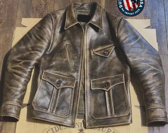 May include: A distressed dark brown leather jacket featuring a pointed collar, a full-length front zipper, and long sleeves with buttoned cuffs. The jacket includes two large lower flap pockets with buttons, a vertical zippered chest pocket, and a small flap pocket.