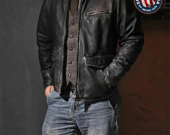 May include: A dark brown distressed leather jacket worn over a brown plaid vest, a dark shirt, and a brown tie, paired with blue denim jeans. A circular badge in the top right corner features an American flag and the text DUTY PAID TO USA.