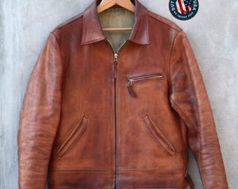 Puede incluir: Una chaqueta de cuero marrón con cuello, cremallera frontal completa y un bolsillo con cremallera en el pecho. La chaqueta presenta mangas largas con puños, dos bolsillos laterales inclinados en la cintura y un acabado texturizado.