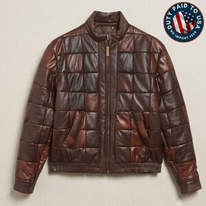 May include: A brown leather jacket featuring a quilted patchwork design with square panels in varying shades of dark and medium brown. The jacket has a stand-up collar, a central gold-tone zipper closure, and two side pockets with a ribbed hem.