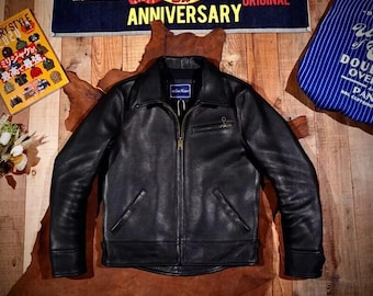 May include: A black leather jacket with a zip-up front, a small chest pocket, and two side pockets. The jacket is displayed on a brown surface with a wooden background. A banner above reads "40 ANNIVERSARY".