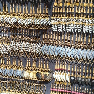 Puede incluir: Una gran colección de pendientes colgantes con ganchos y aros de metal dorado. Los diseños incluyen varias formas geométricas, triángulos y elementos circulares hechos de materiales estampados, rayados y de colores sólidos.