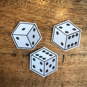 May include: Three white dice with black dots, each in a hexagonal shape, are arranged on a wooden surface. The dice show different numbers: one, five, and six. The dice are outlined in black.