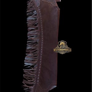 May include: Brown leather chaps with decorative floral tooling at the top and long fringe along the sides. The chaps have a Western Apparel logo and are designed for showmanship.