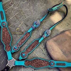 Può includere: Un set di briglie per cavalli in pelle turchese e marrone con intricate incisioni floreali e finiture argentate. Il set include una capezzina, una fronte e una sottogola, con dettagli decorativi turchesi. L'immagine include anche il testo "WESTERNAPPARELLS".