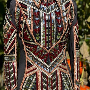 May include: A black long-sleeve show shirt featuring a high collar and a front zipper. The garment is heavily embellished with geometric patterns of red, gold, and clear crystals, rhinestones, and metallic studs arranged in intricate designs.