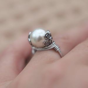May include: A silver ring with a white pearl and a decorative swirl design.