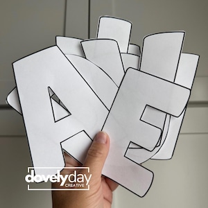 May include: A stack of white paper letters with bold black outlines, featuring the letters A and E prominently in the front. The letters are cut out in a block font style. The logo for dovelyday CREATIVE is printed in white on the bottom left.