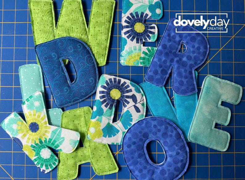 May include: A collection of fabric letters spelling out words, featuring various patterns in shades of blue, green, and teal. The letters include floral prints, polka dots, and swirls. The logo for dovelyday creative is visible in the top right corner.