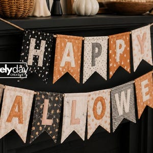 May include: A fabric banner spelling HAPPY HALLOWEEN with individual pennants in black, orange, and cream patterns. Each pennant features a letter in a contrasting color. The text "dovelyday CREATIVE" is printed on the left side of the banner.