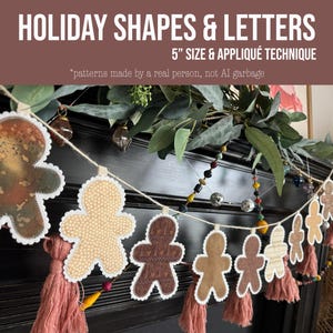 May include: A garland featuring multiple gingerbread man shapes in various brown and beige fabric patterns, each with white scalloped edges. The shapes are strung on a cord with pink tassels hanging between them, measuring 12.7 cm in size.
