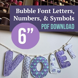 以下が含まれることがあります： 6インチのバブルフォントの文字、数字、記号のデジタルPDFダウンロード。画像には、紫とティールの様々なパターンでVIOLETと綴られた布製の文字が、糸の収納棚がある壁を背景に白い紐に吊るされている様子が写っています。