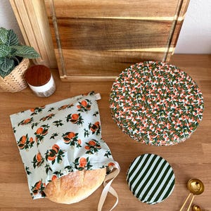 May include: A light blue bread bag with orange and green fruit print, a round lid with a green and white striped pattern, and a round lid with a red and green floral pattern. Wooden cutting boards and measuring spoons are also visible.