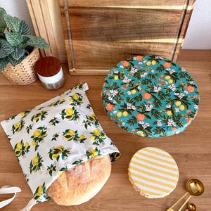 May include: A loaf of bread in a white bag with a lemon print, and two round food covers with floral and striped patterns. Wooden cutting boards and measuring spoons are also visible.