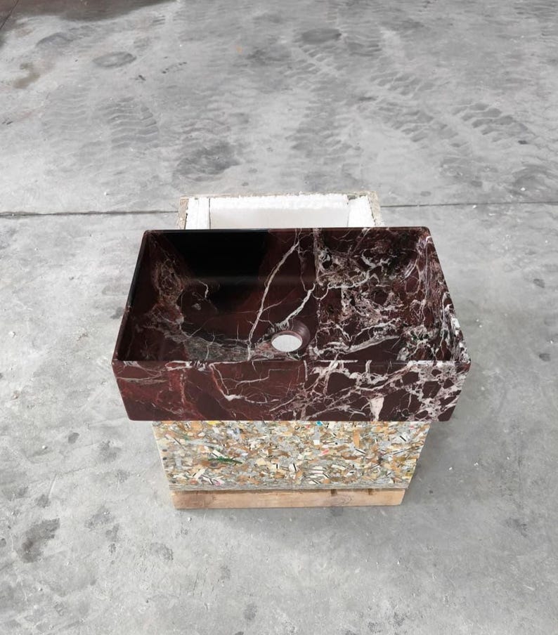 May include: A rectangular, burgundy marble sink with white veining. The sink has a single drain hole and is displayed on a wooden pallet. The sink's rich color and unique pattern make it a striking bathroom fixture.