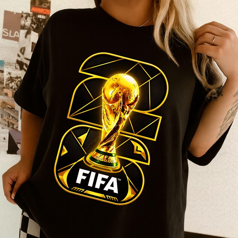 以下が含まれることがあります： 金色のFIFAワールドカップトロフィーのデザインが施された黒いTシャツ。デザインにはFIFAのロゴと2022の数字が幾何学的なスタイルで含まれています。このシャツは半袖のクルーネックです。