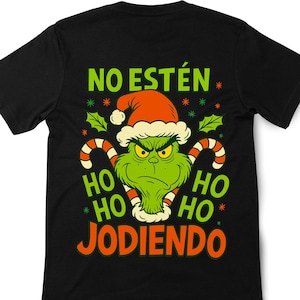 Puede incluir: Camiseta negra con un personaje verde del Grinch con un gorro de Papá Noel, y el texto "NO ESTÉN JODIENDO" en verde y naranja. El diseño incluye bastones de caramelo y detalles festivos.