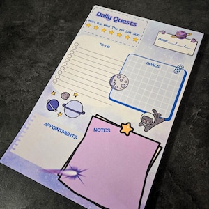 May include: A notepad with a space theme, featuring a purple and blue color scheme. The notepad includes sections for daily quests, to-do lists, appointments, goals, and notes. Decorative elements include planets, stars, and a space cat.