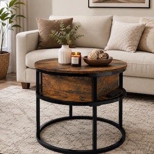 May include: A round coffee table with a dark wood grain top and a black metal frame. The table features a central storage compartment and a lower circular base. On the surface sits a white ribbed vase with greenery, a candle, and a wooden bowl.