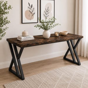 May include: A rectangular desk with a dark brown wood grain finish and a black metal frame featuring X-shaped legs. The desk surface holds a stack of two books, a white ceramic vase with green foliage, a glass candle holder, and a beige bowl.