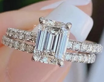 May include: A two-piece diamond ring set. The engagement ring features an emerald-cut diamond center stone. The band and the ring are encrusted with smaller diamonds. The rings are silver in color.