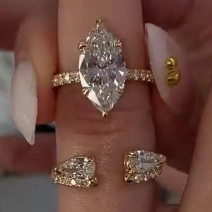 May include: A gold ring set featuring a large marquise-cut center stone on a pavé band and a separate open-style band with two pear-cut stones. The text OUR DESIGN to give your engagement ring is visible at the top of the image.