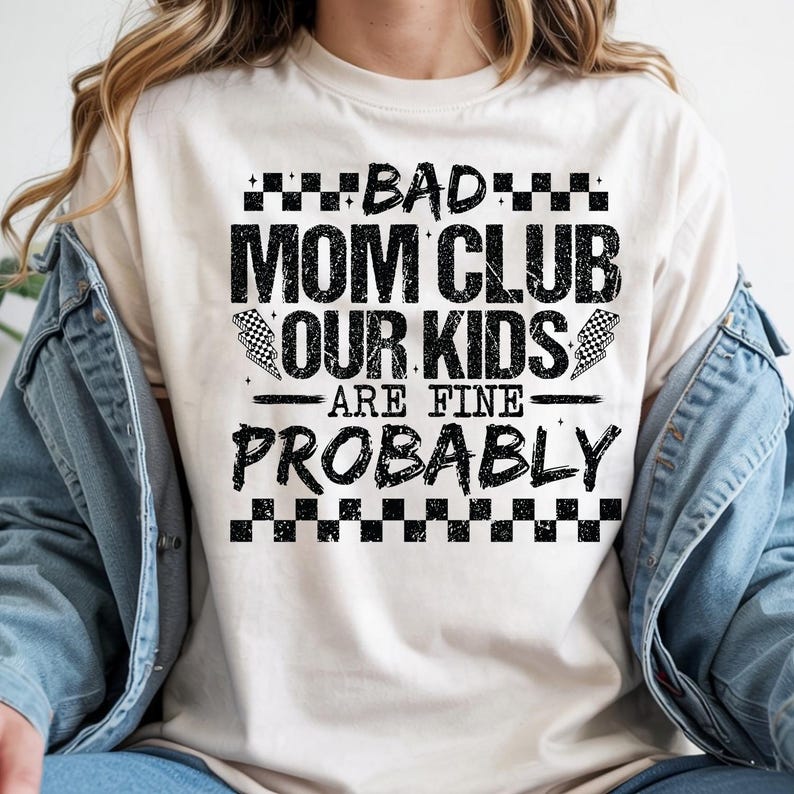 May include: Cream-colored t-shirt with the text "BAD MOM CLUB OUR KIDS ARE FINE PROBABLY" in black block letters. The design includes checkered flag graphics and a checkered border at the top and bottom of the text.