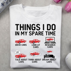 Puede incluir: Camiseta blanca con el texto "THINGS I DO IN MY SPARE TIME" e ilustraciones de coches clásicos rojos. La camiseta enumera actividades relacionadas con los coches.