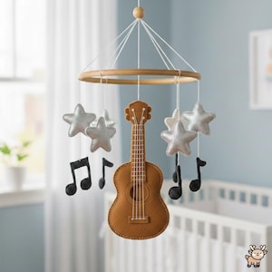 Pode incluir: Um móbile suspenso para quarto de bebé com uma guitarra central de feltro castanho, rodeada por estrelas de feltro prateado e notas musicais pretas suspensas numa moldura circular de madeira por fios brancos.