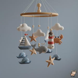 May include: A nautical-themed mobile featuring felt shapes suspended from a circular wooden frame. The hanging elements include white clouds, tan starfish, a blue and white striped sailboat, a grey whale, a red and white lighthouse, and a crab.