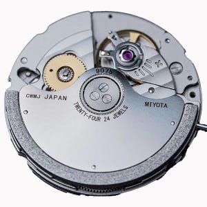 K&ouml;nnte beinhalten: Nahaufnahme eines Uhrwerks mit sichtbaren Zahnr&auml;dern, Schrauben und einer Unruh. Der silberfarbene Mechanismus zeigt die Schriftz&uuml;ge "CWMJ JAPAN", "MIYOTA" und "TWENTY-FOUR 24 JEWELS". Ein komplexes mechanisches Ger&auml;t.