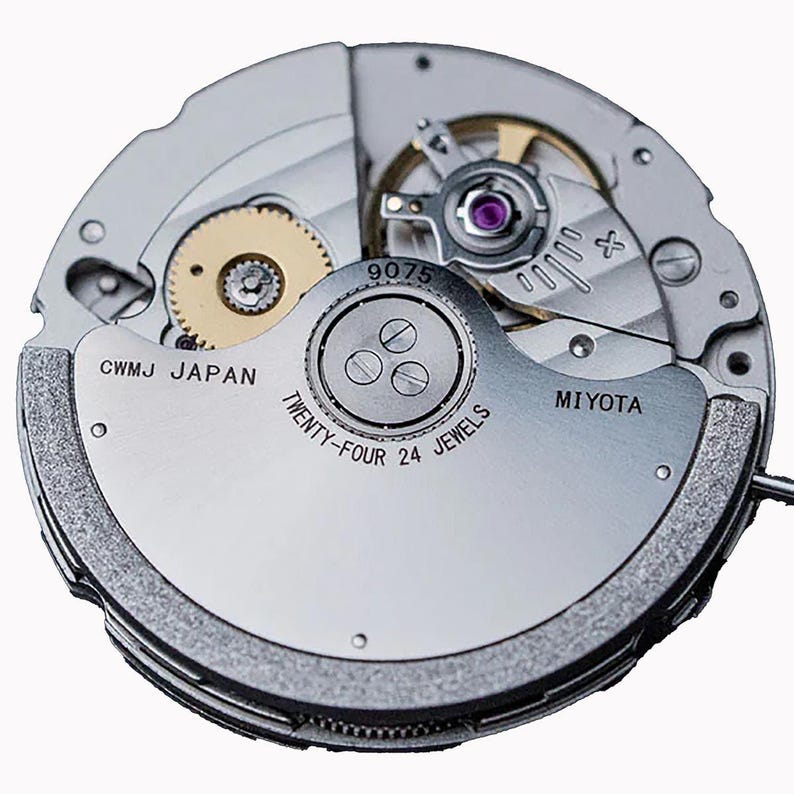 K&ouml;nnte beinhalten: Nahaufnahme eines Uhrwerks mit sichtbaren Zahnr&auml;dern, Schrauben und einer Unruh. Der silberfarbene Mechanismus zeigt die Schriftz&uuml;ge "CWMJ JAPAN", "MIYOTA" und "TWENTY-FOUR 24 JEWELS". Ein komplexes mechanisches Ger&auml;t.