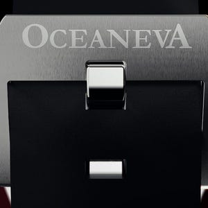 K&ouml;nnte beinhalten: Nahaufnahme einer Uhrenschlie&szlig;e mit dem Markennamen "OCEANEVA" auf einer geb&uuml;rsteten Metalloberfl&auml;che eingraviert. Der Verschluss ist schwarz mit einer silberfarbenen Schnalle und einer rechteckigen &Ouml;ffnung.