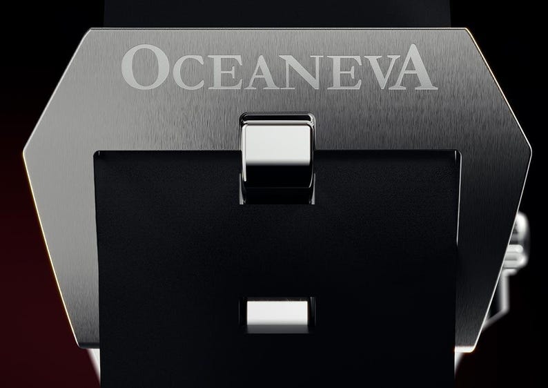 K&ouml;nnte beinhalten: Nahaufnahme einer Uhrenschlie&szlig;e mit dem Markennamen "OCEANEVA" auf einer geb&uuml;rsteten Metalloberfl&auml;che eingraviert. Der Verschluss ist schwarz mit einer silberfarbenen Schnalle und einer rechteckigen &Ouml;ffnung.